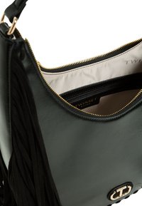 Čierna kožená kabelka so zlatými kovaniami, zapínaním na zips a strapcovými detailmi. Vo vnútri má béžovú podšívku a ďalší vrecko na zips.