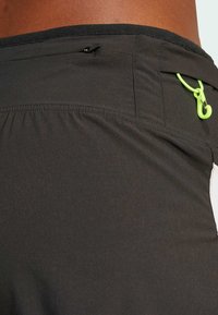 Svarta träningsshorts med en slät yta, elastisk midjeband och en liten ficka med dragkedja som har en grön dragtab.