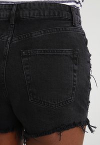 Černé džínsové šortky s třepeným lemem, s jednou zadní kapsou a strukturovaným pasem. Látka má texturovaný povrch.