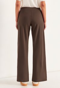 Bruine, wijde broek met een zachte textuur en een elastische tailleband, gedragen met een lichtgekleurde, kortemouwen shirt en beige schoenen.
