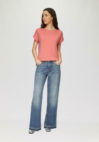 Koralowa bluzka z krótkim rękawem i podwiniętymi rękawami, zestawiona z jasnoniebieskimi spodniami dzwonami, charakteryzującymi się prostym krojem i delikatnym przetarciem. Srebrne buty dopełniają całość.