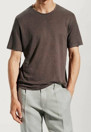 T-shirt marron à manches courtes avec un col rond, fabriqué en matériau doux, porté sur un pantalon gris clair, avec une coupe décontractée.