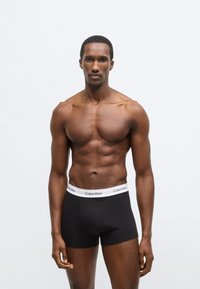 Μαύρα ανδρικά εσώρουχα boxer με λευκή μέση που φέρει το λογότυπο "Calvin Klein". Το ύφασμα φαίνεται λείο και η εφαρμογή είναι στενή στο σώμα.