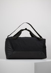 Czarna torba sportowa wykonana z trwałego materiału, z płaskim dnem, dwoma uchwytami na górze i regulowanym paskiem na ramię dla większej uniwersalności.