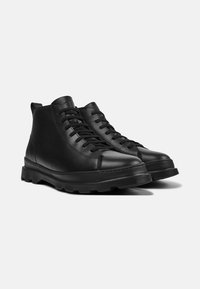 Botas de cuero negro hasta el tobillo con puntera redondeada, suela de goma resistente y cordones planos. Cuenta con un lazo en la parte posterior para ponérselas fácilmente.