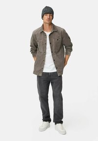 Grå kordfløjlsjakke med to brystlommer, kombineret med en hvid T-shirt og mørkegrå jeans. Modellen bærer en mørk strikket hue og hvide sneakers.