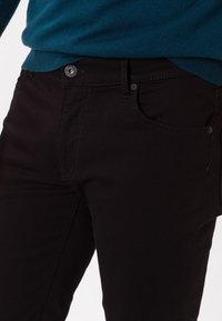 Jeans in denim nero con una vestibilità slim. Presentano una tasca frontale, chiusura con bottone e cuciture a contrasto. Texture liscia e colore uniforme.