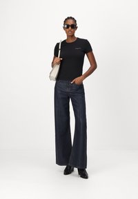 Černé přiléhavé tričko, tmavé volné džíny s viditelnými švy a černé kotníkové boty. Malá světle šedá taška s popruhem a sluneční brýle.