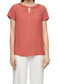 Top corto a maniche corte corallo con collo rotondo, dettagli decorativi con tagli e tessuto morbido e leggero; vestibilità leggermente rilassata.