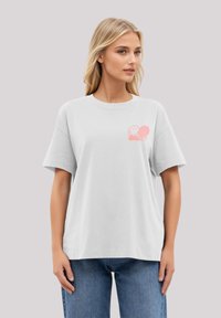 Übergroßes, hellgraues T-Shirt aus Baumwolle mit einem pinken Smiley-Gesicht-Graphic auf der linken Brustseite und kurzen Ärmeln.