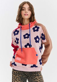 Farebná mikina s kapucňou s ružovým základom a námorníckymi kvetinovými vzormi, červenými rukávmi a korálovou klokankou, ktorá má modrý akcent.