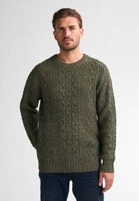 Oliwkowy, dzianinowy sweter z teksturowanymi splotami warkoczowymi, okrągłym dekoltem i ściągaczami. Materiał wydaje się gruby i ciepły.