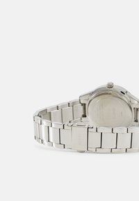 Montre en acier inoxydable avec un bracelet poli, un boîtier rond et une couronne simple. Le dos présente une gravure de la marque et des informations sur la résistance à l'eau.