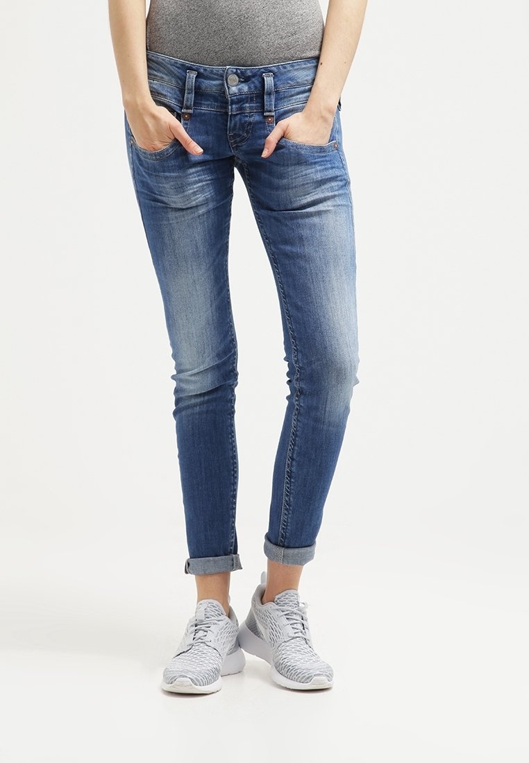 Hoikaty blauw denim broek met gescheurde details, twee voorzakken, een knoopsluiting en opgerolde manchet, gecombineerd met grijze sneakers.