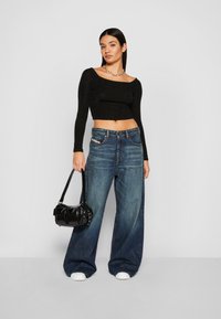 Fekete, csillogó, hosszú ujjú crop top, amelyet világoskék, bő nadrággal párosítanak. A modell egy kis, fényes fekete kézitáskát tart. A megjelenést fehér sportcipők egészítik ki.