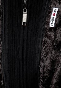 Chaqueta negra con cremallera, de textura suave y aterciopelada en el exterior, con forro interior acanalado, cremallera metálica y una etiqueta que dice "we ❤️ vintage".