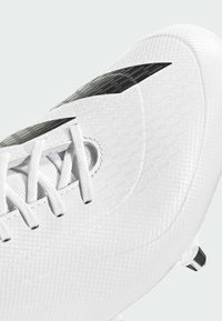 Valkoinen jalkapallokengä, jossa on teksturoitu pinta, mustat yksityiskohdat ja valkoiset nauhat. Varustettu kuudella nappulalla, jotka tarjoavat pitoa nurmikolla.