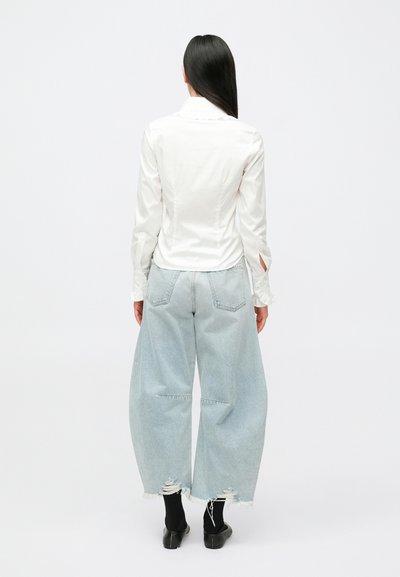 Camisa branca de manga comprida com silhueta ajustada e punhos abertos, combinada com jeans de perna larga azul claro, com bainha desgastada e bolsos traseiros.