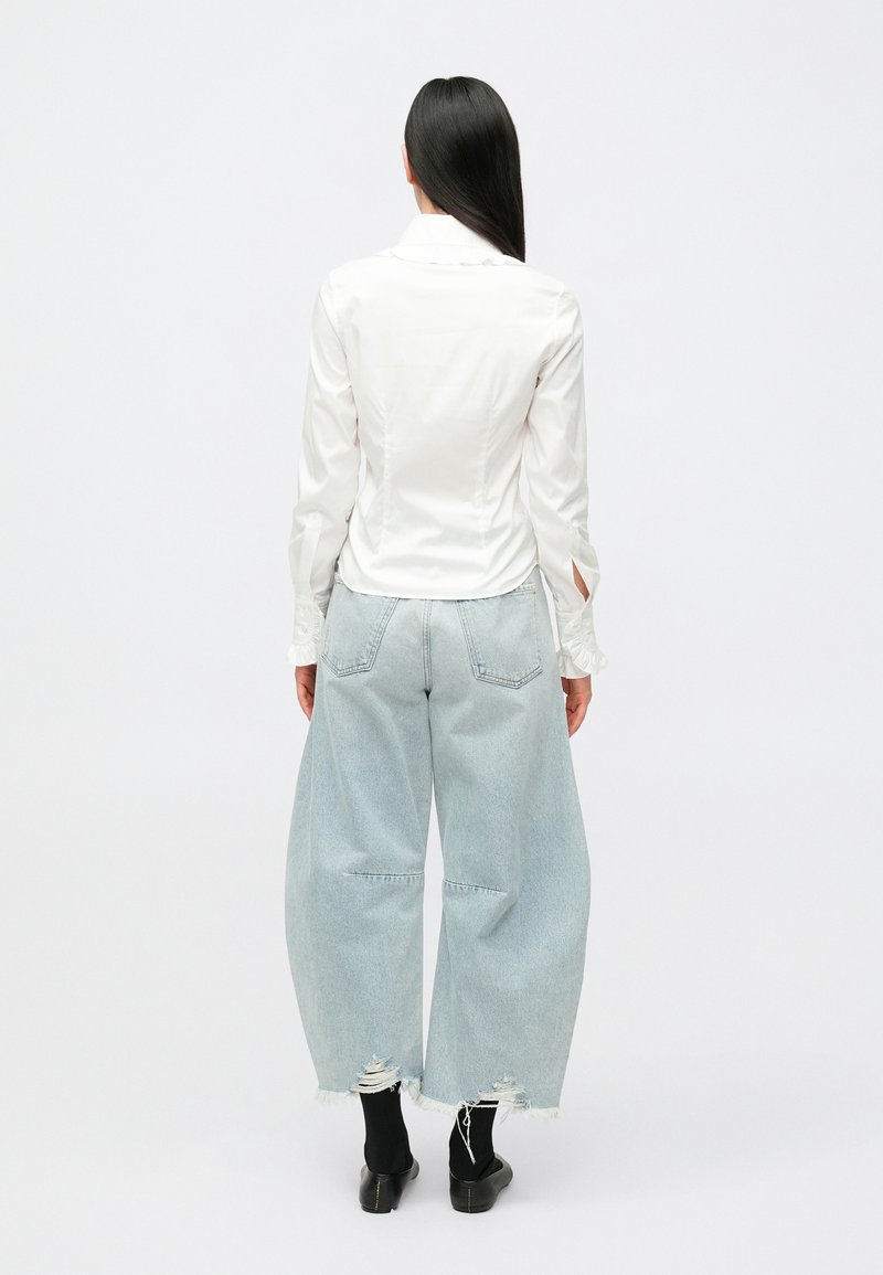 Vitt långärmat linne med figurnära silhuett och öppna manschetter, kombinerat med ljusblå vidbenta jeans med slitna fållar och bakfickor.