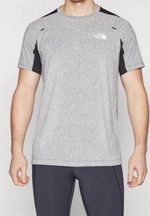 Mężczyzna w jasnoszarej sportowej koszulce z krótkim rękawem, czarnymi bocznymi panelami i logo The North Face na piersi.