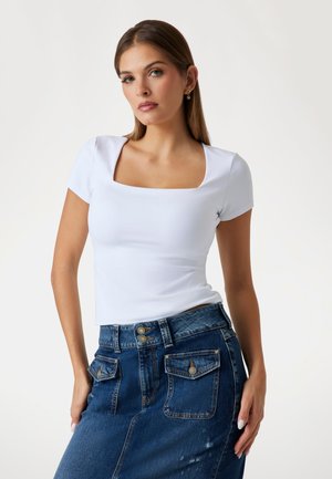Top bianco aderente con scollo quadrato e maniche corte, abbinato a una gonna di jeans a vita alta con due tasche posteriori e bottoni.