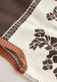 Close-up of a knitted fabric with brown and white floral patterns and a ribbed, folded edge in reddish-brown color.