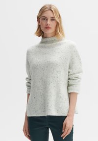 Hellgrüner Pullover mit hohem Kragen, gerippter Textur und gesprenkeltem Muster. Hat hochgekrempelte Ärmel und einen lockeren Schnitt.