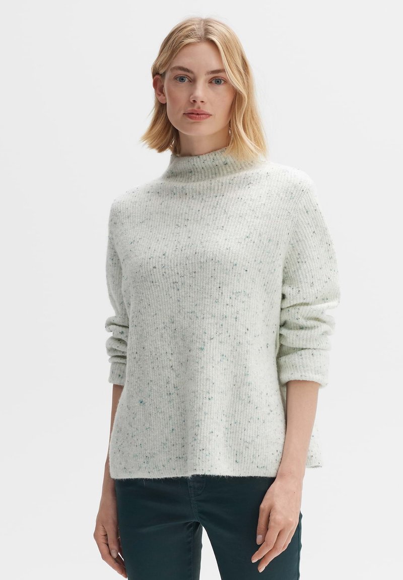 Hellgrüner Pullover mit hohem Kragen, gerippter Textur und gesprenkeltem Muster. Hat hochgekrempelte Ärmel und einen lockeren Schnitt.