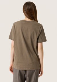 Brun bomull t-shirt med korta ärmar och rund hals; slät textur; har en enkel, odekorerad design på ryggen.