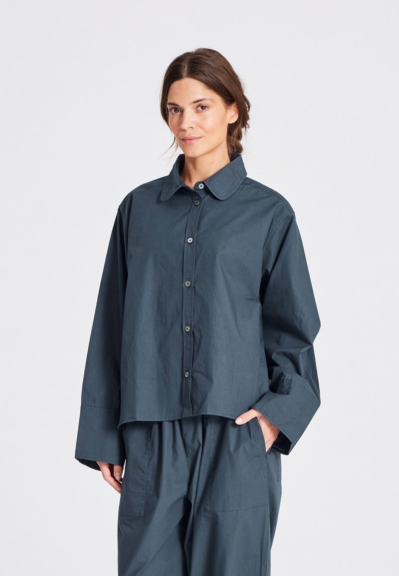 Camicia blu scuro con bottoni realizzata in tessuto leggero, con colletto a punta, ampie maniche e vestibilità comoda.