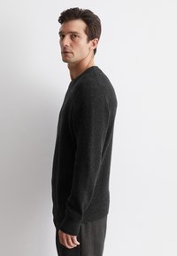 Dunkelgrauer Strickpullover mit V-Ausschnitt, gerippter Textur und langen Ärmeln, kombiniert mit dunklen Hosen, seitlich gegen einen weißen Hintergrund präsentiert.