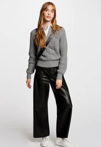 Pull en maille grise avec des poignets côtelés, associé à un pantalon large en faux cuir noir et des baskets blanches. Sac bandoulière noir simple.