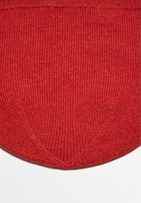 Tessuto a maglia rosso a coste con punta triangolare sul fondo. La trama è morbida e leggermente elastica, offrendo una finitura senza soluzione di continuità.