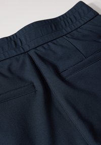 Marineblauwe broek met een brede elastische tailleband, twee achterzakken en een gladde, gestructureerde stof.