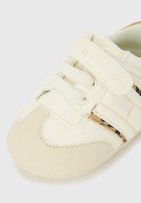 Sneaker per bambini di colore beige chiaro con finitura in pelle liscia, linguetta in rete, lacci elastici e logo sulla fascia. Suola in gomma testurizzata.
