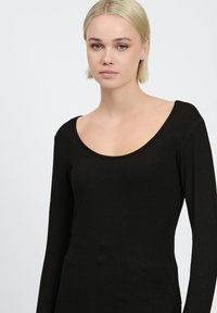Maglietta nera a maniche lunghe con scollo rotondo. Realizzata in un tessuto morbido e elasticizzato, presenta una silhouette aderente e cuciture minime.