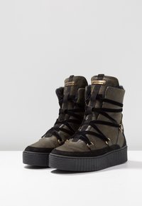 Bottes montantes vert foncé en cuir texturé et en daim, dotées de lacets noirs, d'accents en métal doré et d'une semelle plate noire striée.