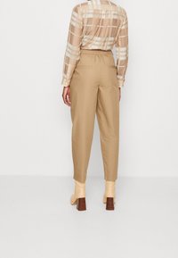 Pantalons beiges avec une taille élastique, présentant une coupe ample et des jambes droites. Portés avec une chemise à carreaux, beige et crème, à boutons et des bottes beiges.