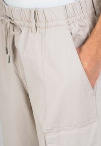 Helle beige Shorts mit einem elastischen Bund und Kordelzug, ausgestattet mit seitlichen Taschen und einem strukturierten Stoff für zusätzliche Details.