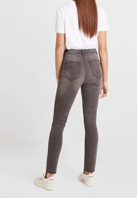 Jeans ajustados de mezclilla de cintura alta en color gris oscuro, con un diseño ceñido, bolsillos traseros, textura suave y con mínimo hardware.