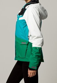 Giacca da sci colorata con un design blu ver turquoise e bianco, con dettagli verdi, cappuccio regolabile e diverse tasche frontali. Logo del marchio in evidenza.