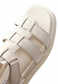 Sandale en cuir blanc avec larges brides et boucle ajustable sur une semelle texturée, vue en gros plan de dessus.