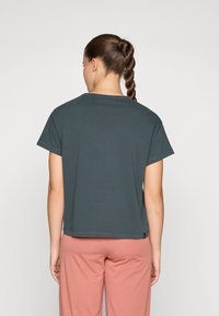 Dark green short-sleeve t-shirt with a relaxed fit, round neckline, and lightly finished edges, paired with light pink pants.