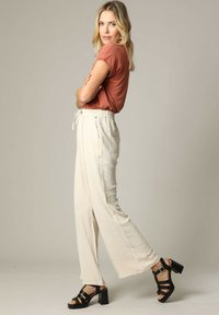 Beige wijde broek met een gestructureerde afwerking, elastische tailleband en koord. Gekoppeld aan een roestkleurig aansluitend t-shirt en zwarte enkelbandhakken.