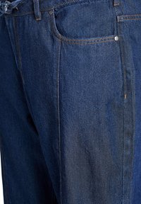 Tamne traperice tamnoplave boje s vidljivim šavovima, dva džepa i teksturiranom završnom obradom. Imaju pojas s vezicom za zatvaranje.