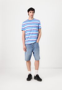 Camiseta a rayas azul con líneas rojas y blancas, combinada con pantalones cortos de mezclilla azul claro. Las zapatillas negras y los calcetines blancos completan el conjunto.