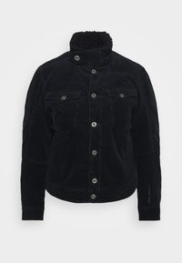 Svart kordjacka med hög krage, två framfickor med lock, silverdetaljer och textil med struktur. Anmärkningsvärd sömdetalj på framsidan.