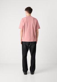 Rosa bomulds t-shirt med rund halsudskæring, korte ærmer og en afslappet pasform, parret med sorte bukser og sorte sko. Bagside.