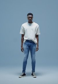 Camiseta de manga corta gris claro, jeans ajustados azules y zapatillas negras altas. Texturas de tela suaves, estilo casual y detalles del ajuste visibles.