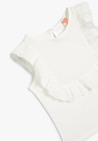 Hvid ærmeløs top med tekstureret stof, der har scallop-lace trim langs skuldrene og en nøglehulslukning bagpå.